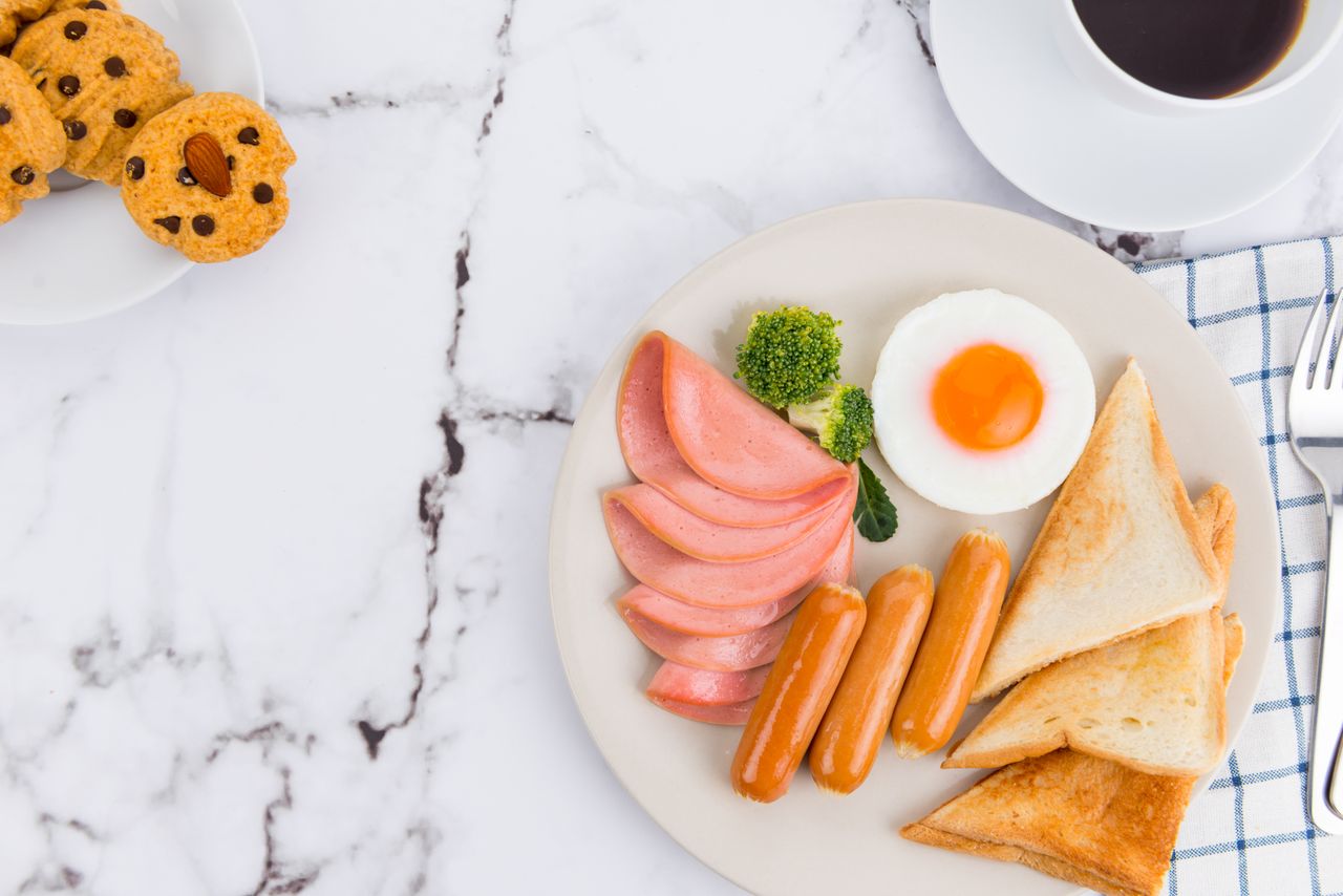 Delicious breakfast of sausages, ham, toast, egg, and coffee on a marble table.